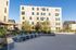 Modern apartment complex with natural wood exterior and spacious communal patio, featuring stylish outdoor seating and lush greenery under a clear blue sky.