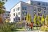 Contemporary apartment buildings with modern wooden siding, surrounded by lush greenery, featuring a family enjoying a walk nearby.