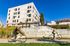 Contemporary apartment building with a modern wooden facade and landscaped surroundings, featuring a path for cyclists under a clear blue sky.
