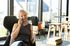 Bright and modern lounge area featuring a smiling woman enjoying a coffee and phone call, surrounded by stylish furniture and natural light.