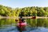 Tranquil lake scene with a kayaker paddling on calm waters surrounded by lush, green forest.