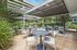 Inviting outdoor patio area with modern seating and string lights, perfect for entertaining and dining. Surrounded by lush greenery, featuring built-in grills for a great barbecue experience.