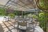 Charming outdoor patio with elegant seating under a pergola, lush greenery, and a sparkling swimming pool.