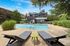 Inviting apartment pool area featuring modern lounge chairs, lush greenery, and a sleek multi-level building backdrop under a brilliant blue sky.