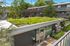 Eco-friendly apartment building with vibrant rooftop garden and inviting patio area, surrounded by lush greenery.