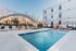 Modern apartment complex featuring a sparkling outdoor pool with stylish lounging chairs and a sleek archway, perfect for relaxation and leisure.
