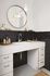 Elegant bathroom featuring a sleek white countertop and modern black subway tile backsplash. Large round mirror and contemporary pendant lights add a touch of sophistication.