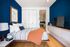 Chic bedroom with bold blue accent wall, cozy striped bedding, sleek modern furniture, and warm wooden flooring.