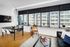 Modern apartment interior with sleek wooden flooring, large windows offering abundant natural light, a stylish dining area, and a cozy seating space.