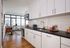 Modern kitchen with sleek white cabinets, black countertops, and natural light pouring in from large windows, featuring a cozy dining area.