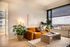 Bright and inviting living area with a cozy orange sofa, modern striped coffee table, and large window offering a stunning city view.