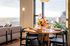 Elegant dining space with wood table set for four, featuring vibrant floral centerpiece and large windows offering stunning cityscape views.