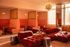 Chic and modern lounge area with vibrant red couches, elegant orange booth seating, and a stylish bubble chandelier, flooded with natural light.