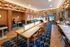 Chic communal workspace featuring modern wooden tables, cozy booths, and vibrant shelving with books and plants.