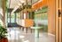 Modern apartment lobby with elegant wood paneling, vibrant green accents, and stylish pendant lighting. Features lush indoor plants and a sleek mailbox area.