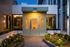 Chic apartment entrance with modern lighting and lush landscaping, showcasing elegant architectural design at dusk.