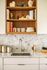 Elegant kitchen countertop with modern faucet, textured backsplash, and open wooden shelving showcasing stylish decor and cookbooks.