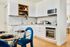 Modern kitchen with sleek white cabinetry, integrated appliances, and a stylish glass dining table with plush blue chairs.