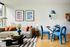 Modern living space with chic grey sofa, vibrant orange pillows, and elegant glass dining set, accented by bold geometric art.