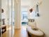 Bright and inviting hallway with cozy seating, stylish hat and bag decor, leading to a sunlit bedroom with city views.