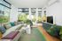 Spacious modern living room with large windows, inviting natural light and offering stunning views of lush greenery, sleek furniture, and vibrant decor.