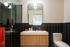 Modern bathroom featuring sleek black tiles, a stylish wooden vanity with a white countertop, and contemporary lighting.