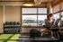 Modern fitness room with panoramic river and bridge view, featuring treadmills, kettlebells, and a variety of equipment for an invigorating workout.
