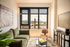 Modern living room with a large window view of a scenic bridge, featuring a stylish green sofa, wooden chair, and chic decor on a plush rug.
