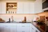 Chic modern kitchen with sleek white cabinets, elegant backsplash, and polished countertops featuring luxurious wooden accents and culinary books.