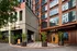 Modern urban building entrance with vibrant greenery and stylish architecture, featuring a trendy grill and bar.