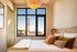Chic bedroom with large windows offering stunning city views, featuring cozy pillows and stylish lighting.