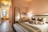 Chic bedroom showcasing a comfortable bed with plush pillows, warm lighting, and sleek wooden accents, leading into a cozy dining area with a modern design.