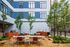 Charming outdoor communal space with stylish seating, lush greenery, and modern grilling stations against a sleek building backdrop.