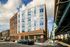 Chic urban apartment building with a vibrant mural facade, located next to a bustling city street and transit line.
