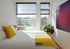 Bright modern bedroom with large windows, vibrant yellow accents, and a lush potted plant, creating a fresh and inviting atmosphere.