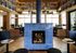 Chic lounge interior featuring a vibrant blue-tiled fireplace, surrounded by cozy seating, lush plants, and stylish shelving with books and decor.