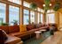 Bright and inviting lounge area with large windows, elegant wooden accents, and cozy seating adorned with colorful cushions. Lush greenery adds a touch of nature to the modern, open-concept space.