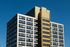 Modern high-rise building with striking golden facade and expansive windows set against a clear blue sky.