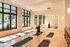 Bright yoga studio with large windows, showcasing natural light and reflections, featuring yoga mats and a person practicing headstand.