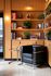 Modern reading nook featuring a sleek black leather chair, wooden bookshelves filled with colorful books and decorative plants, and a stylish glass side table.