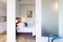 Modern apartment interior featuring a cozy bedroom with contemporary lighting, fresh blue accents, and frosted glass doors opening to a sleek kitchen area.