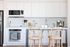 Elegant modern kitchen with sleek white cabinetry, premium stainless steel appliances, and a cozy breakfast bar with stylish wooden chairs.