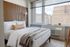 Elegant bedroom with modern wood paneling and large windows showcasing a stunning city view, offering a bright and serene atmosphere.