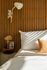 Elegant bedroom corner featuring a white pillow against a modern wooden slat wall, with warm lighting and a cozy decorative cushion.
