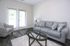 Bright and cozy living room with modern furniture, featuring a plush gray sofa, stylish armchair, and a sleek glass coffee table on beautiful wood flooring.