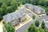 Aerial view of modern apartment complex with ample parking, surrounded by lush greenery, showcasing a welcoming community atmosphere.