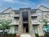 Charming three-story brick apartment building with elegant balconies, beautifully landscaped with lush greenery and vibrant balloons, under a clear blue sky.