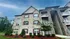 Charming apartment building with modern brick facade, elegant balconies, and lush landscaping under a bright blue sky.