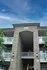 Inviting apartment complex entrance with elegant stone facade and charming balconies, set against a vibrant blue sky.
