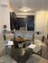 Modern apartment dining area with a glass table set for four, facing a sleek open kitchen with elegant dark wood cabinets and stainless steel appliances.